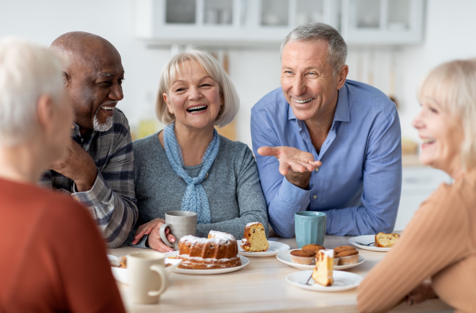 A group of older adults sitting around a table, eating and enjoying afternoon tea while smiling and chatting with each other.