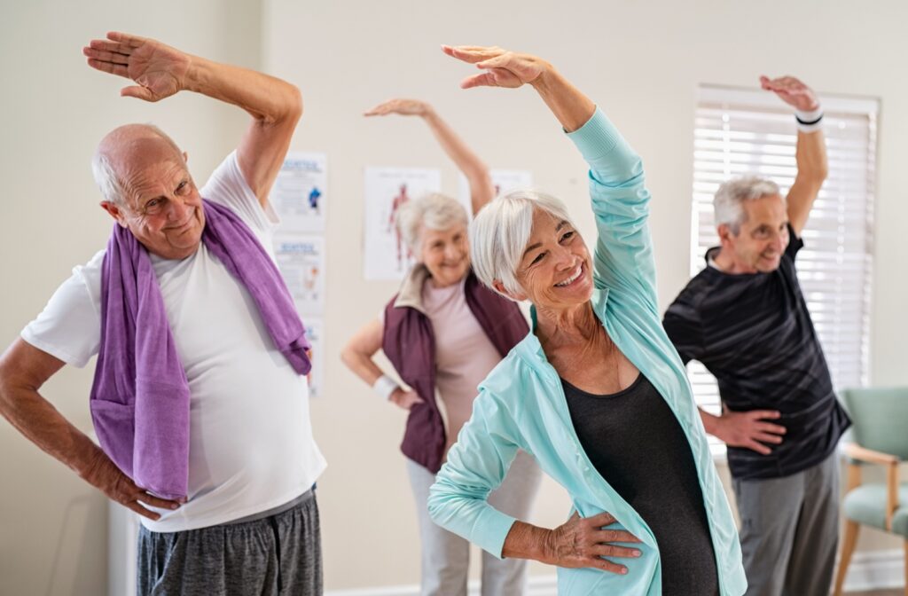 A group of older adults in an exercise class smiling and stretching.