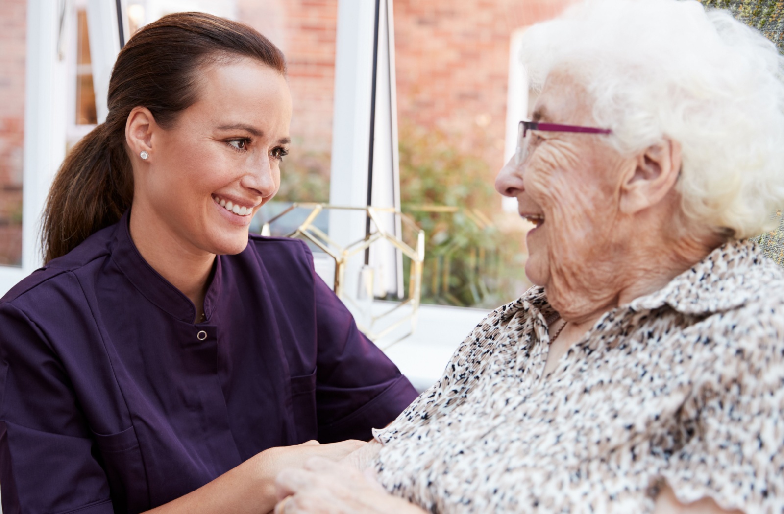 A female caregiver laughing and visiting with an older adult woman at a senior living community.