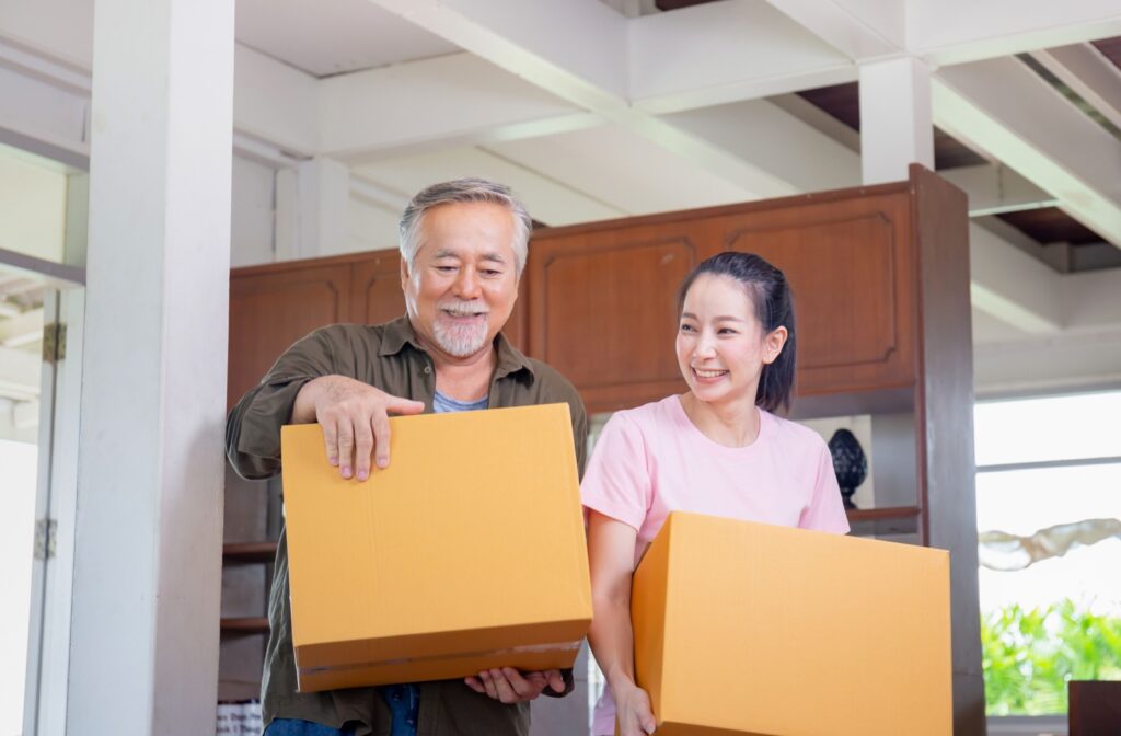 An older man and his daughter carrying moving boxes and smiling.