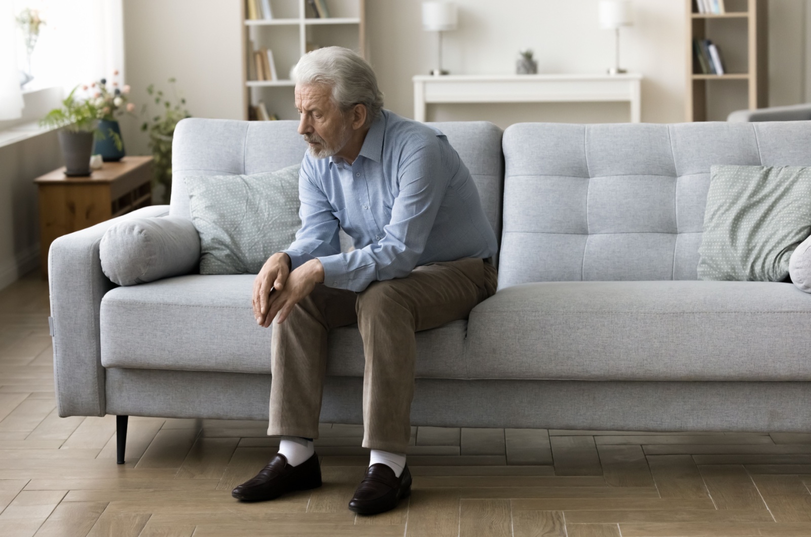 An older adult sitting on the couch alone at home, suffering from social isolation.