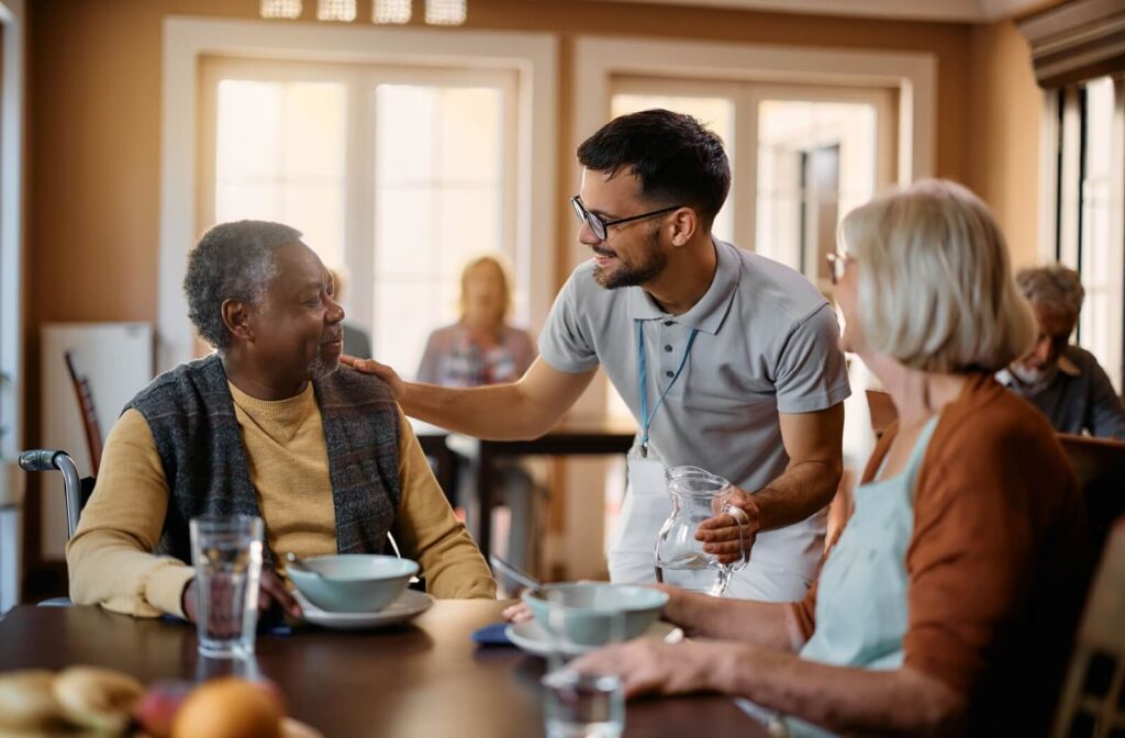 A caregiver checking in on 2 residents of assisted living during a group breakfast.