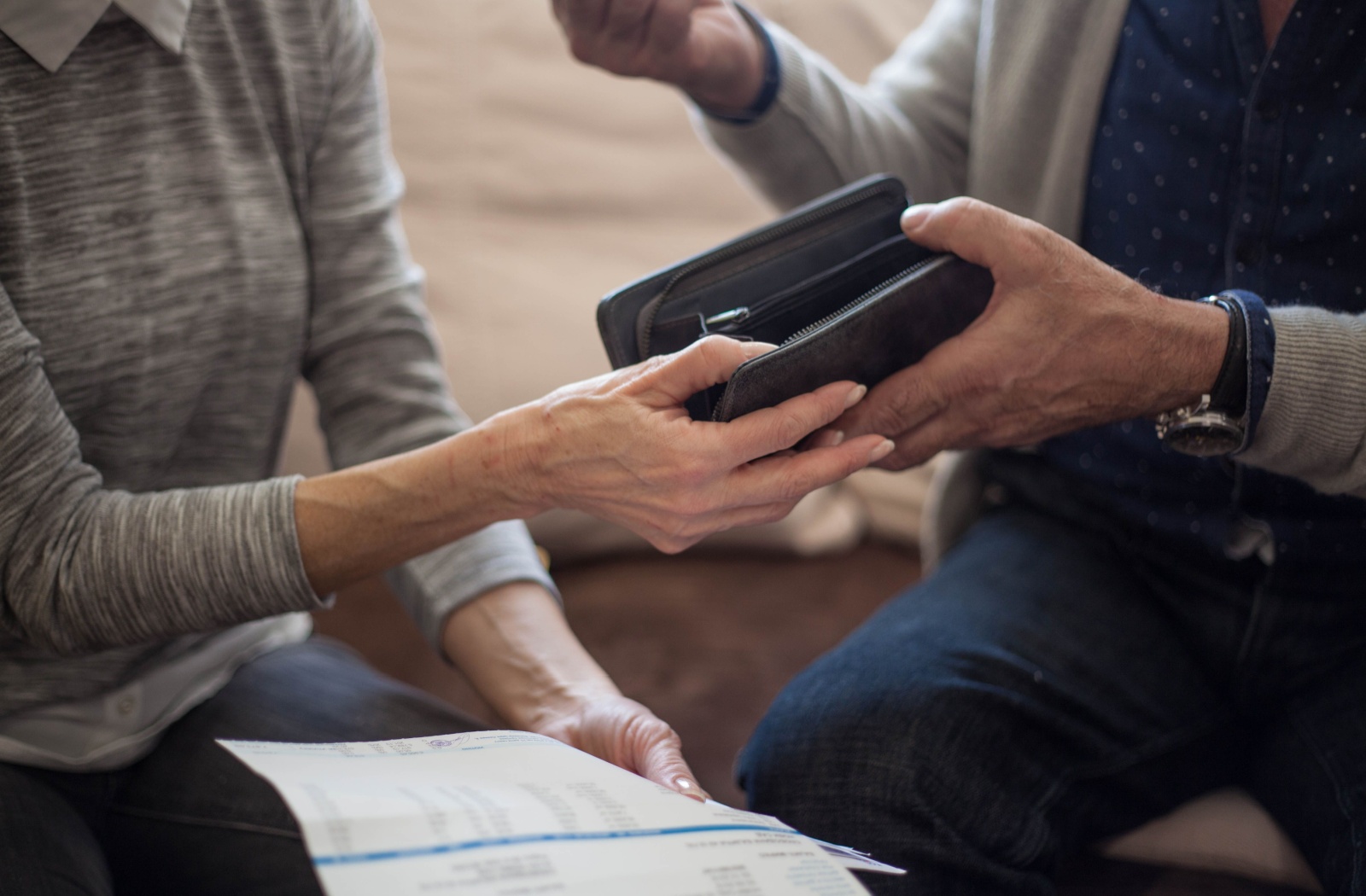 An older adult handing their partner their wallet to reduce the risk of spending money.