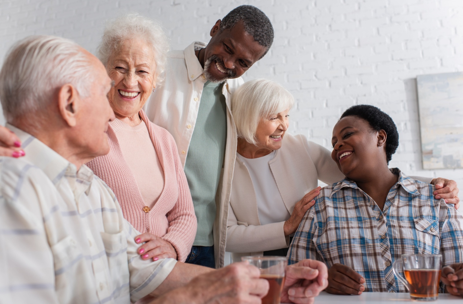A group of seniors say hello in a communal space in assisted living, chatting over afternoon tea