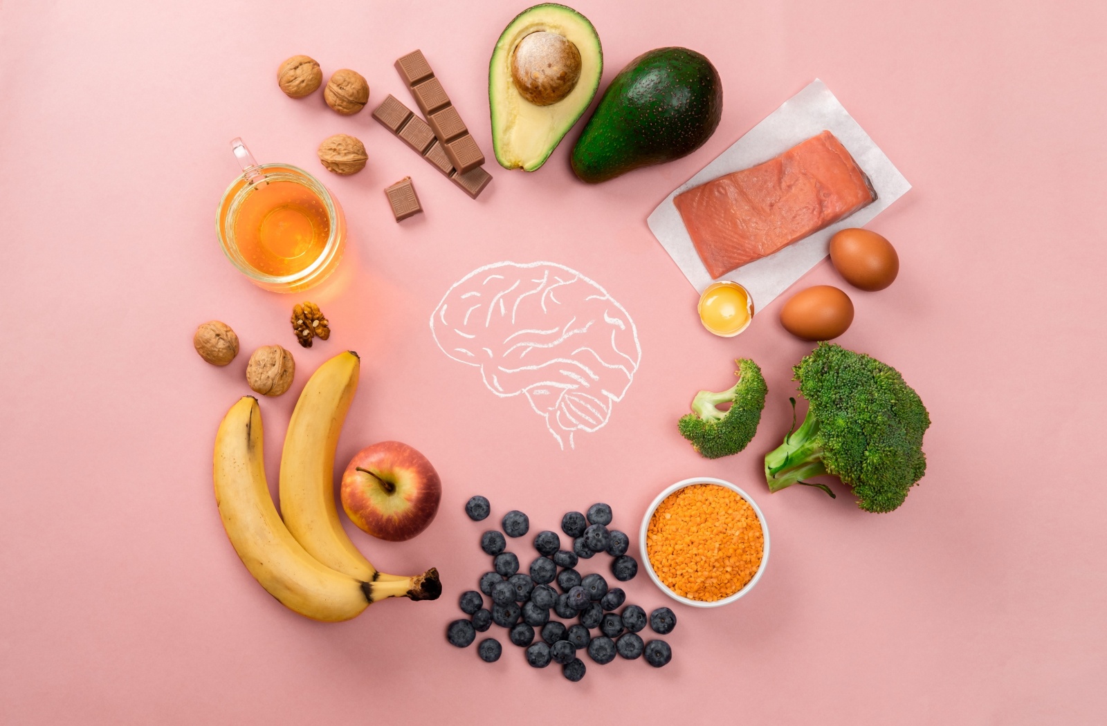 Against a pink background, several healthy foods, including berries, salmon, and broccoli, surround a visual of a brain