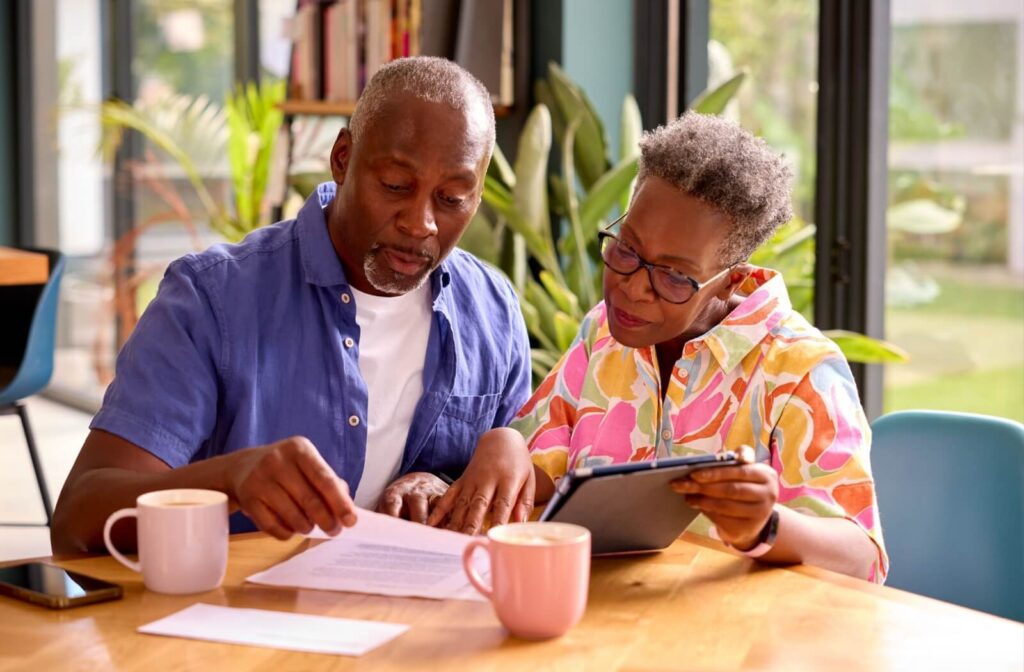 A senior couple reviews paperwork with their online banking to make a budget for affording assisted living