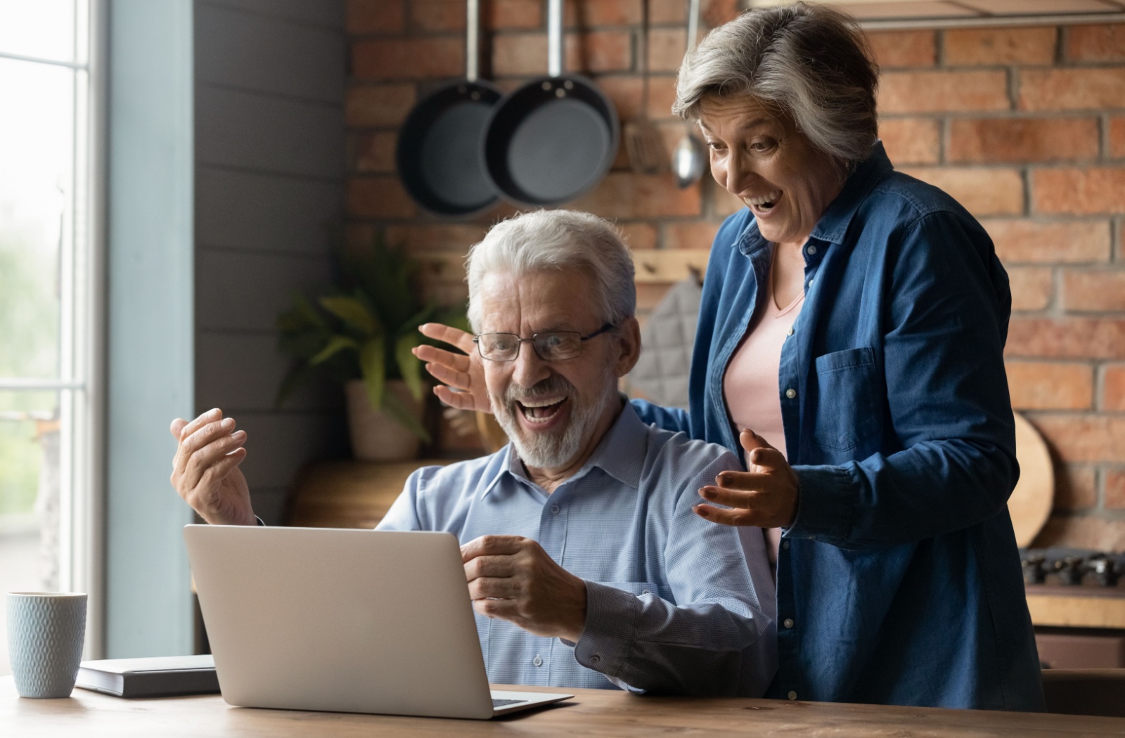 An older couple laughing with excitement while they look at images of a senior living community on their laptop in their kitchen