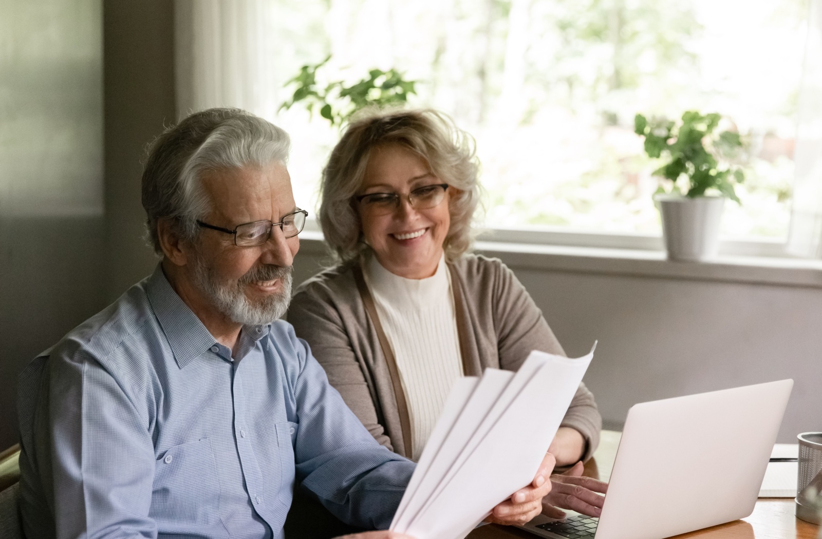 An older couple focuses on paperwork while reading from their laptop during the application process for senior living