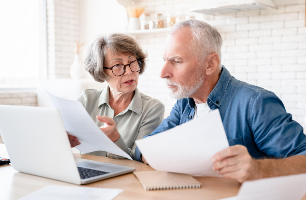 An older couple focuses on paperwork while reading from their laptop during the application process for senior living