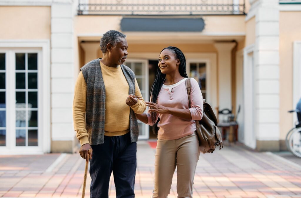 An adult and their senior parent stand outside an assisted living community, preparing to go on a tour together